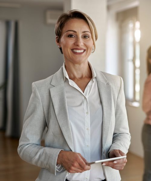 Portrait of happy real estate agent looking at the camera while her clients are standing in the background.